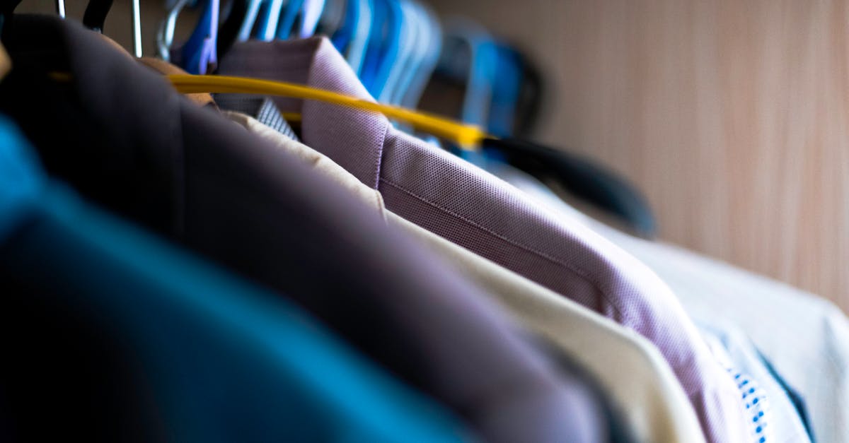 Close-up of various shirts hanging on colorful hangers inside a wardrobe.
